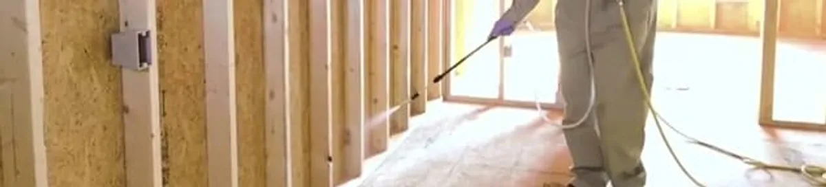 Termite treatment technician applying spray along framing and unfinished walls in Orlando, FL